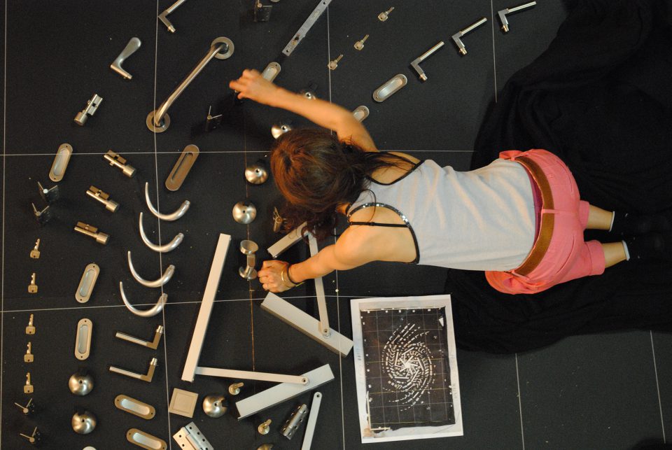 Ein Foto der Künstlerin Sarah Illenberger, wie sie gerade ein Motiv aus Türklinken auf dem Boden zusammenstellt.