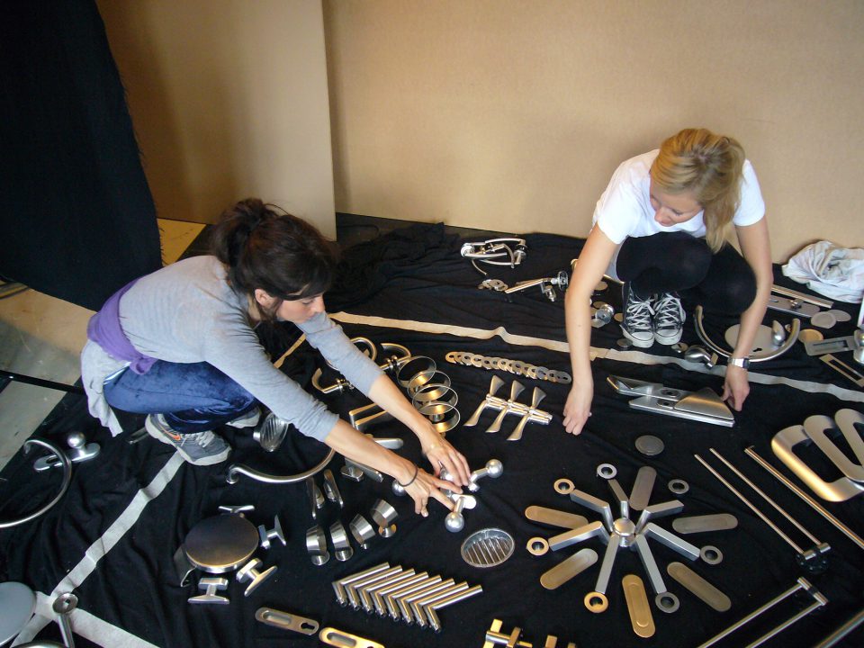 Ein Foto der Künstlerin Sarah Illenberger, wie sie ein Motiv aus Türklinken auf dem Boden zusammenstellt.